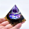 A hand holds a dark pyramid crystal with an amethyst sphere and gold glitter decoration.