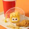 A yellow squeeze toy keychain is displayed on a white plate next to french fries and fried chicken.