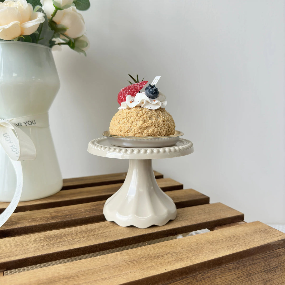 A small cupcake with cream and berries is displayed on a white pedestal stand.