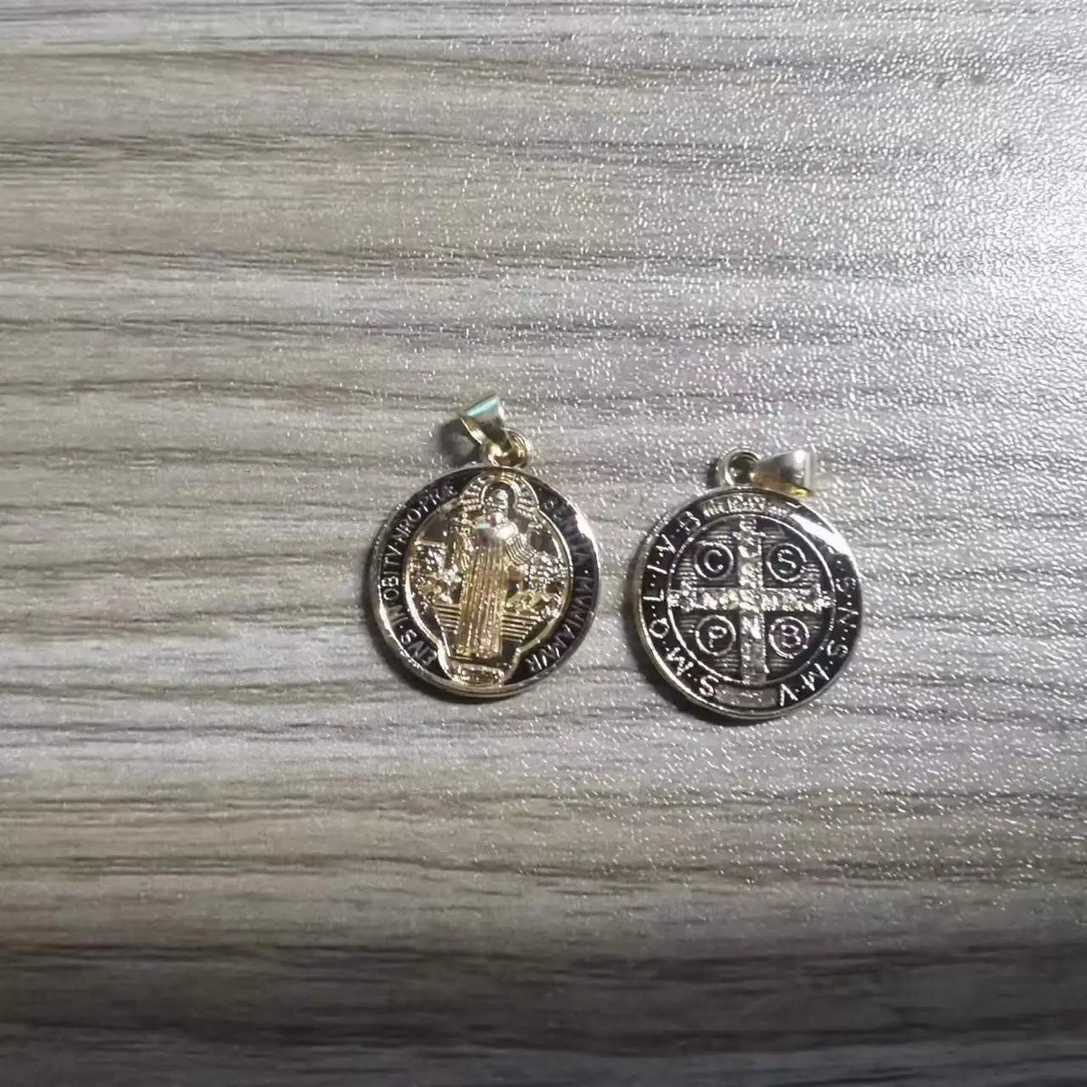 A pair of silver-toned religious pendants featuring St. Benedict imagery and dates.