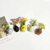 A collection of mini ceramic vases with artificial flowers in yellow, pink, and white on a white background.