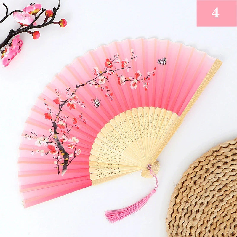 Pink and white floral design silk bamboo folding hand fan with a woven straw mat in the background