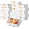 A stack of white kraft paper gift boxes tied with gold ribbon, with one box open displaying a jar.