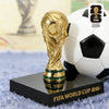 A gold FIFA World Cup trophy figurine displayed on a black base next to a white and black soccer ball.