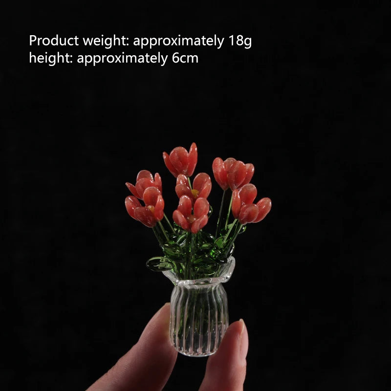 A hand holds a small glass vase filled with red-orange handmade glass flowers.