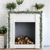 Artificial eucalyptus leaf garland draped over a white fireplace mantel decorated with greenery.