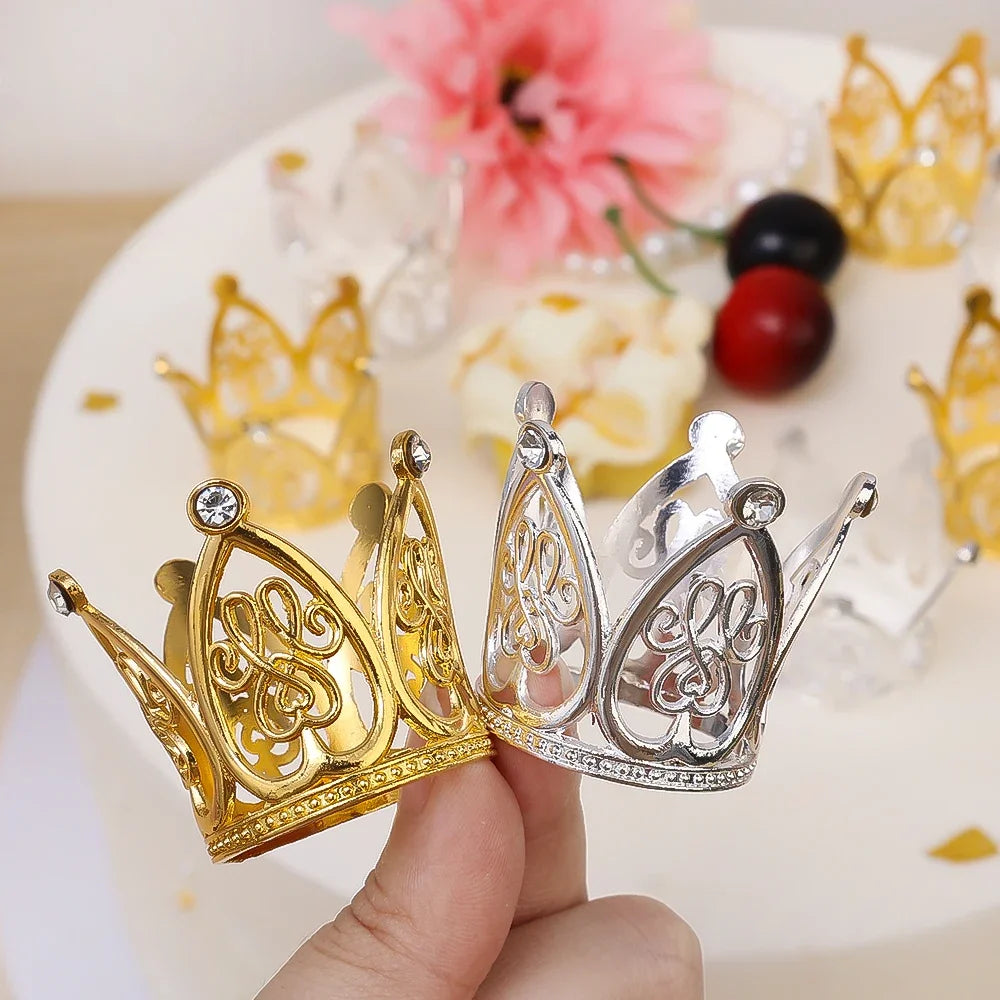 A hand holds a silver and gold mini pearl crown cake topper decoration on a white cake.