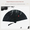 A black folding hand fan with delicate white bamboo patterns is shown in a close-up shot.