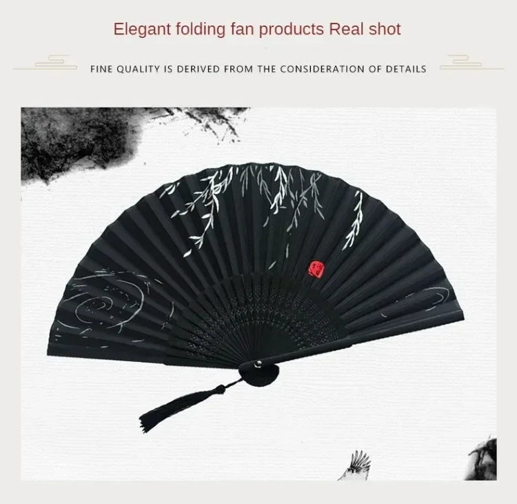 A black folding hand fan with delicate white bamboo patterns is shown in a close-up shot.