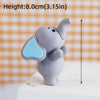 A small gray cartoon elephant cake topper with light blue ear detail, shown standing on a white surface.