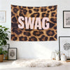 A large tapestry wall hanging featuring the word SWAG in large pink letters on a brown leopard print background.