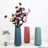A modern, ribbed teal plastic flower vase with dried flowers and pink foliage on a white surface.