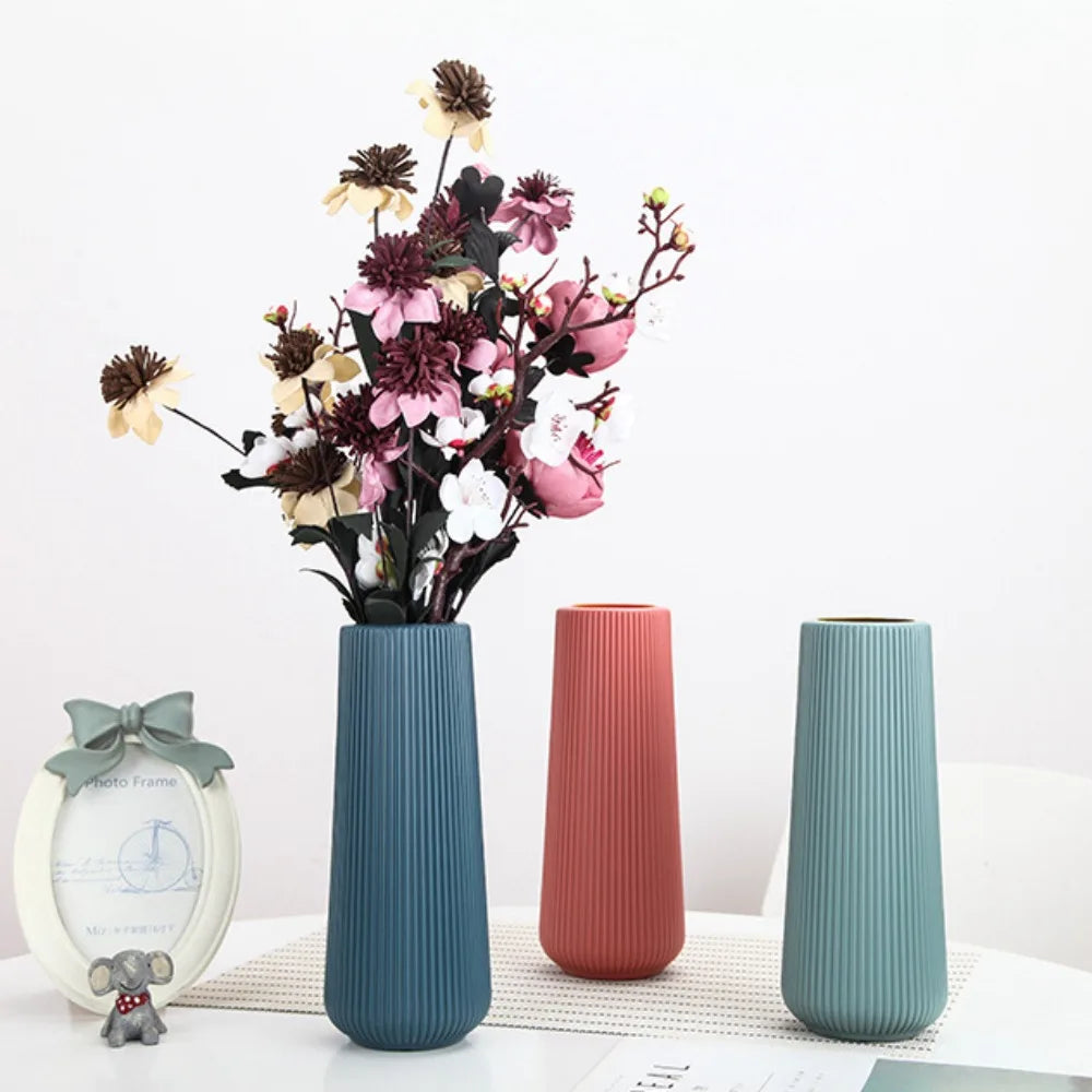 A modern, ribbed teal plastic flower vase with dried flowers and pink foliage on a white surface.