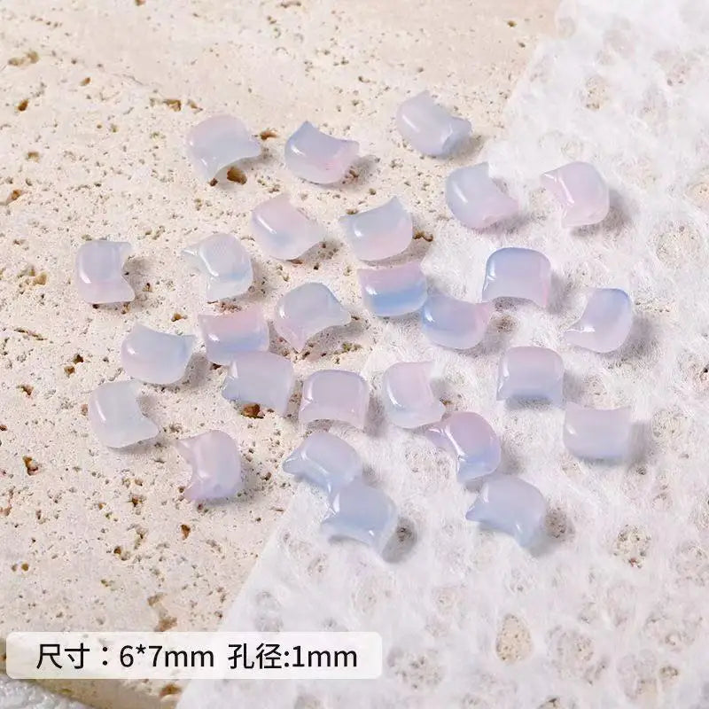 A collection of translucent purple and pink cat head glass beads for jewelry making scattered on a white surface.