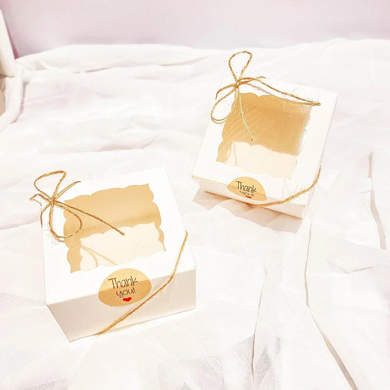Two small kraft paper favor boxes tied with twine and featuring a thank you tag on white fabric