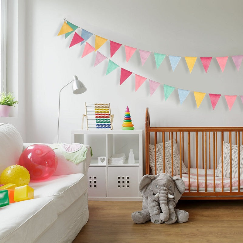 A colorful jute linen pennant banner set strung across a white wall in a nursery room.