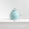 A light blue ceramic mini vase with a rounded body and a narrow opening, shown on a white shelf.