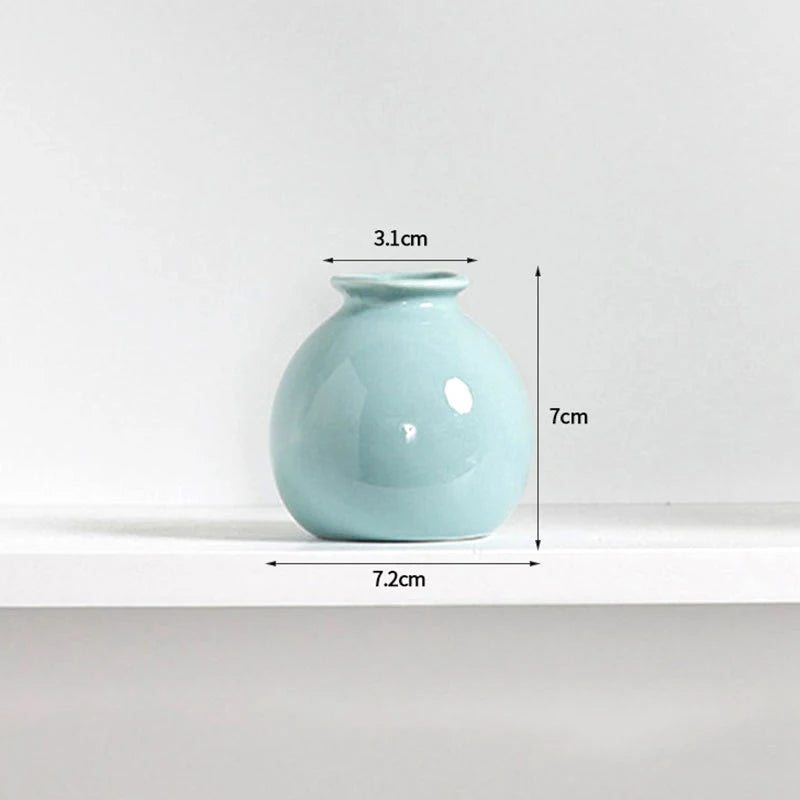 A light blue ceramic mini vase with a rounded body and a narrow opening, shown on a white shelf.