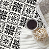 A close-up of a black and white Moroccan pattern floor sticker design on a white background with a cup and a woven basket.