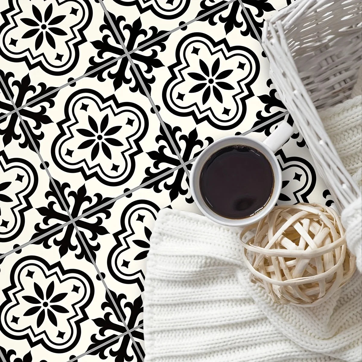 A close-up of a black and white Moroccan pattern floor sticker design on a white background with a cup and a woven basket.