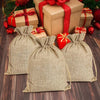 Three natural burlap drawstring bags with red ribbon accents are displayed next to wrapped gifts.