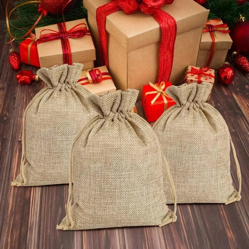 Three natural burlap drawstring bags with red ribbon accents are displayed next to wrapped gifts.
