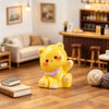 A yellow resin cat keychain with pink accents sitting on a wooden floor.