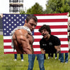 A muscular man stands in front of an American flag banner with red and white stripes and blue stars, featuring a gym theme.