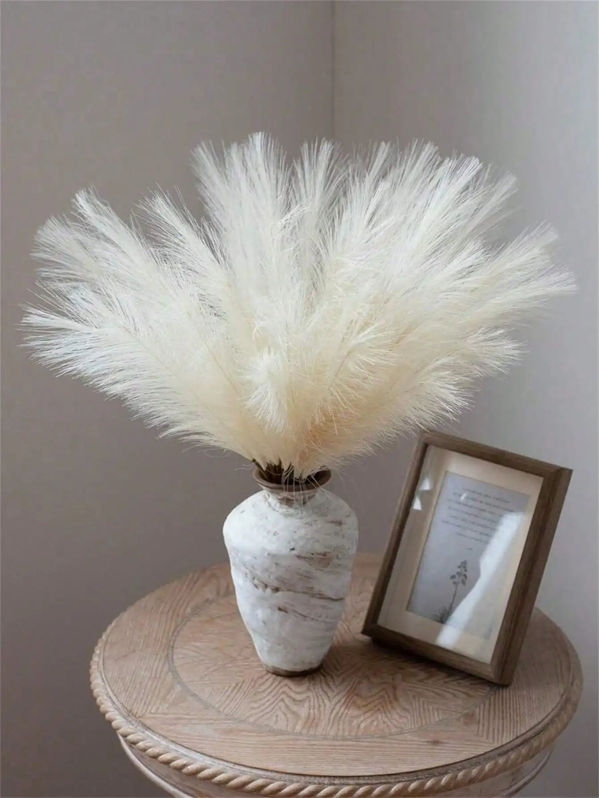 A bundle of fluffy white pampas grass stems displayed in a textured vase on a wooden surface.