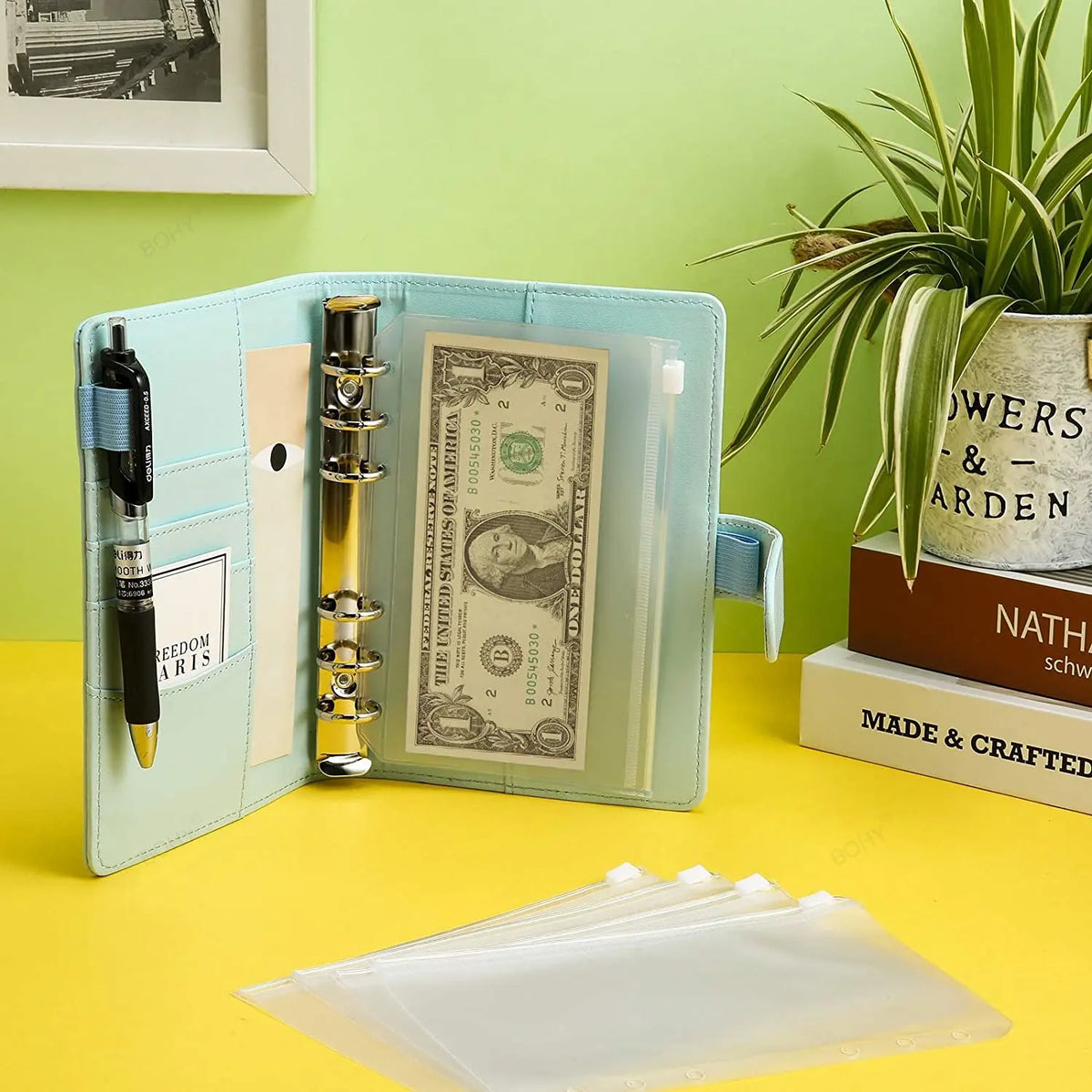 A light blue A6 PU leather budget planner binder with cash envelopes and expense sheets displayed on a yellow surface.