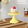 A yellow mini cupcake stand displaying a small cake topped with whipped cream and a strawberry.