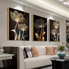 A set of three abstract flower canvas wall art pieces featuring golden and black tones displayed in a modern living room.