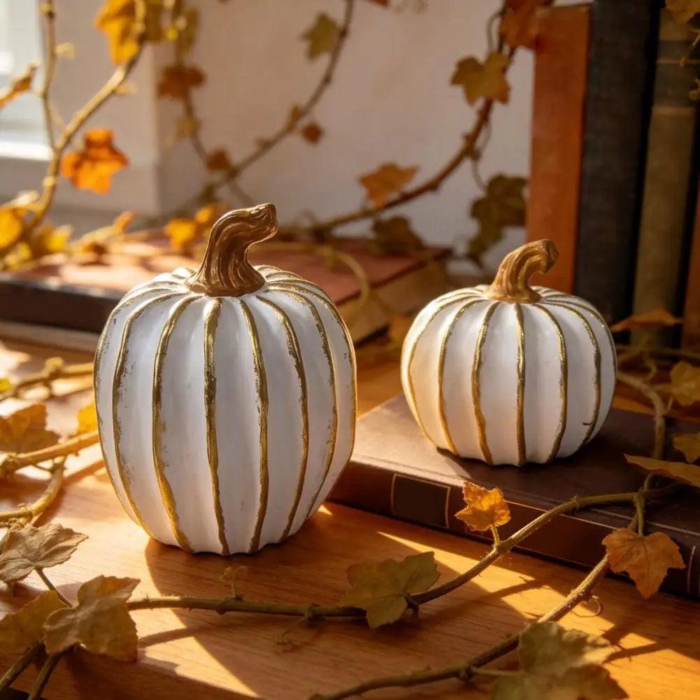 Elegant white and gold resin decorative pumpkins resting on a wooden surface surrounded by autumn leaves.