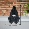 Black resin statue of a ghost with a tea cup on a ledge against a brick wall.