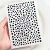 A hand holds a white sheet with black glitter gems arranged in a grid pattern for facial tattoos.