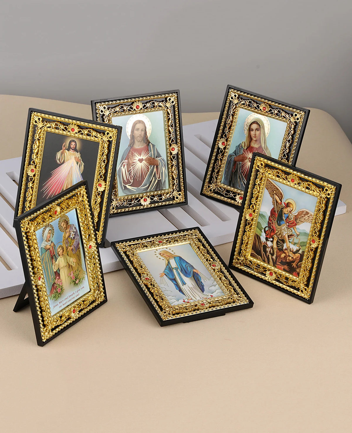 A collection of framed Catholic icons featuring Jesus, Mary, and the Archangel St. Michael on a light-colored surface.