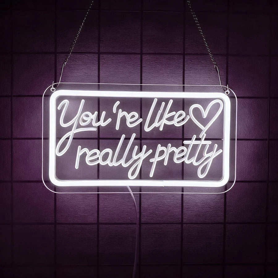 A glowing neon sign hangs against a dark purple grid background, displaying the text You're like really pretty with a heart.