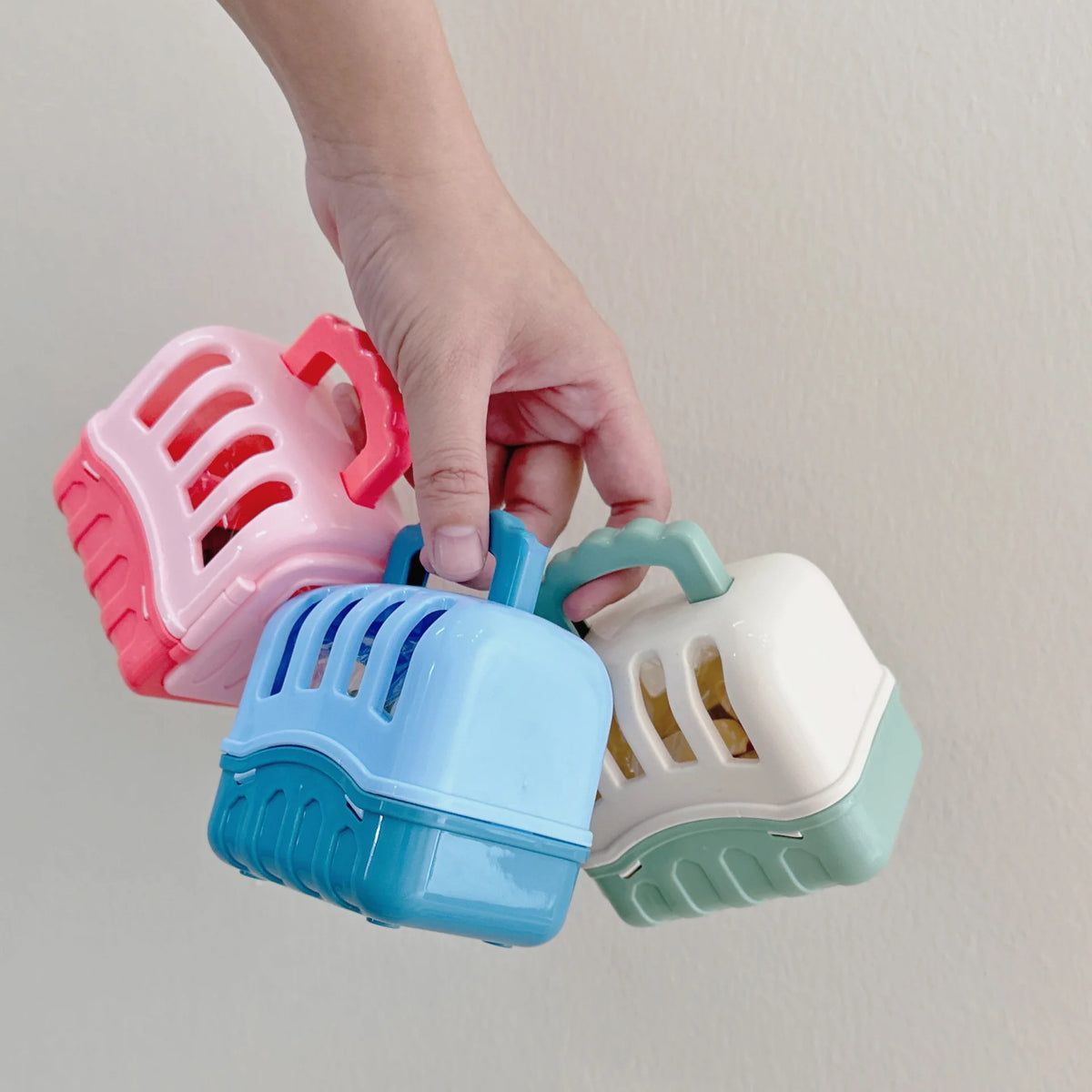 A hand is holding a pink plastic dog basket toy set with various colored baskets.