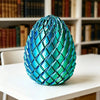 A vibrant blue, textured dragon egg fidget toy resting on a white table in front of bookshelves.