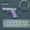A purple miniature handgun model is attached to a silver keyring, shown next to a ruler.