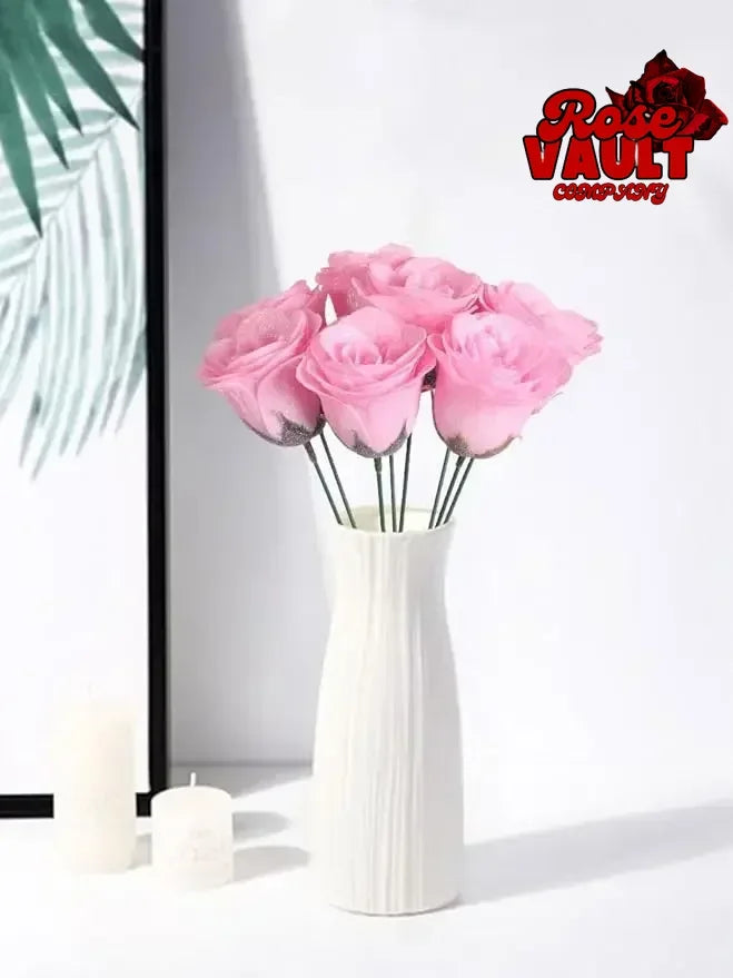 A bouquet of pink artificial roses in a white vase displayed on a white surface.