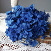 A dense bouquet of vibrant blue dried hydrangea florets resting on a white lace fabric.