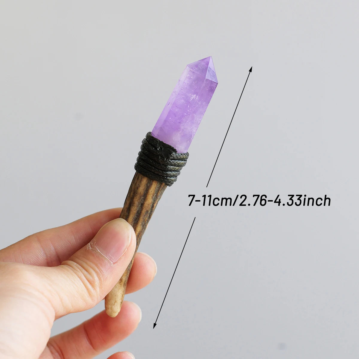 A hand holds a natural purple crystal scepter wand with a pointed termination, showing its length.