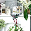 A clear glass bubble balloon filled with decorative elements, including a miniature house and floral greenery.