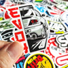 A hand holds a die-cut vinyl decal sticker featuring a stylized white car headlight design with red accents.
