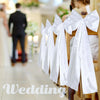 Présentation de grands nœuds de mariage en satin blanc accrochés sur un porte-servi à bois dans un intérieur lumineux.