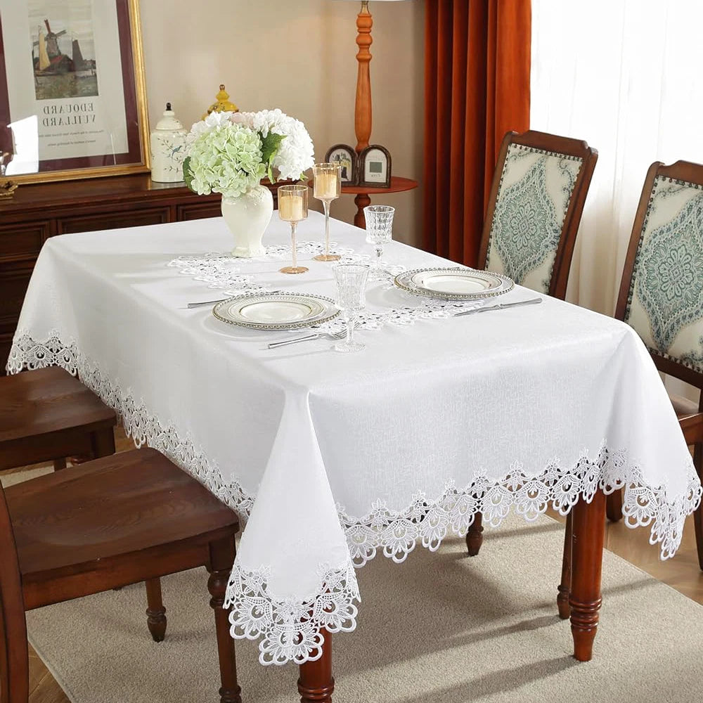 A white embroidered lace tablecloth is set for a meal on a wooden table with floral accents.