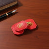 A red felt turtle charm with gold detailing rests on a wooden surface next to a black pen.