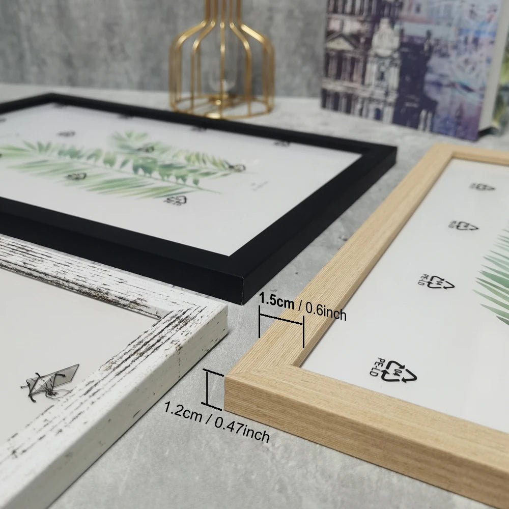 A set of wooden photo frames with black and light wood borders and greenery designs displayed on a gray surface.
