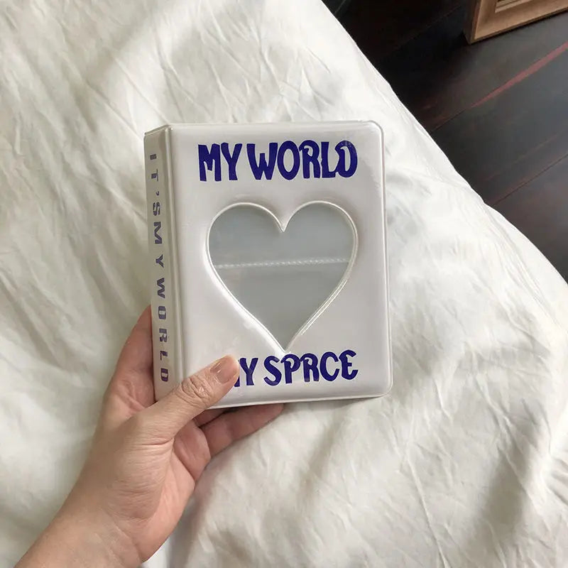 A white photo album titled My World with a heart cutout and the words My Space is held in a hand on a white bed sheet.